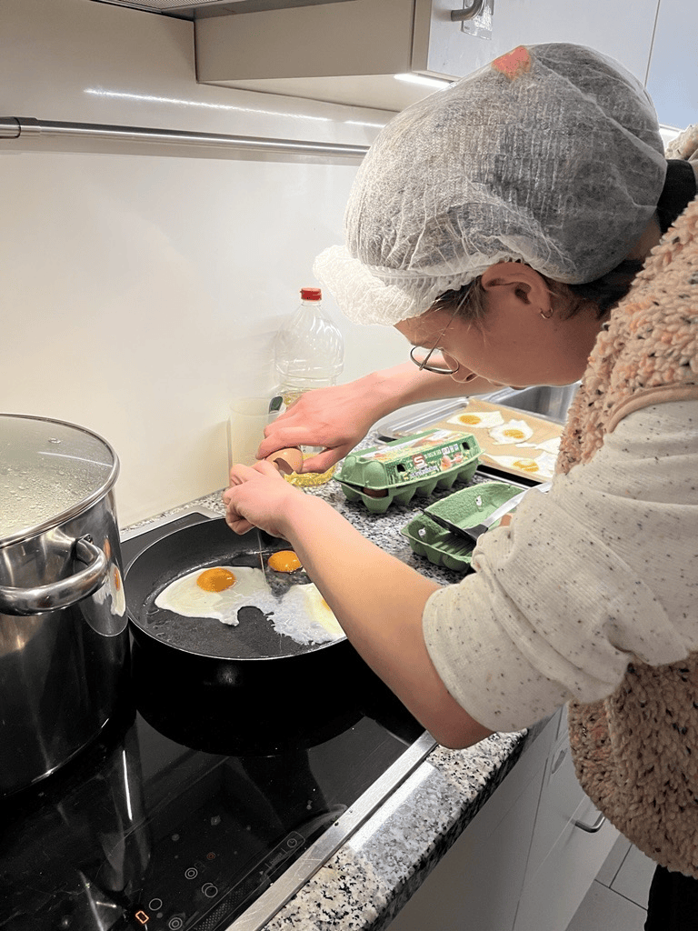 Klientin in der Kochgruppe schlägt ein Ei in eine Pfanne.