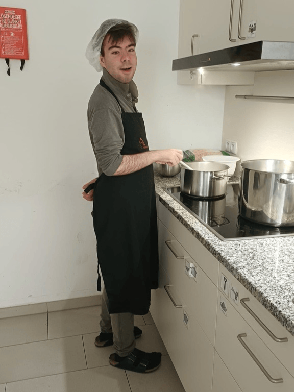 Klient mit Kochhaube und Schürze beim umrühren in einem Kochtopf.